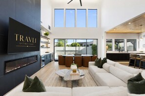 A modern living room with a fireplace, a large TV, and a dining area with round tables and chairs.