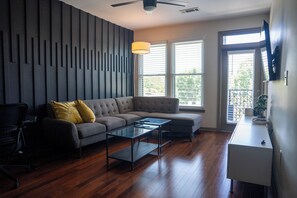 Una sala de estar moderna con un sofá seccional, una mesa de centro de vidrio y una mesita auxiliar blanca.