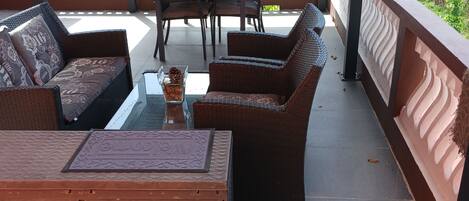 A covered outdoor seating area with wicker furniture, a table, and chairs, overlooking a lush green landscape.