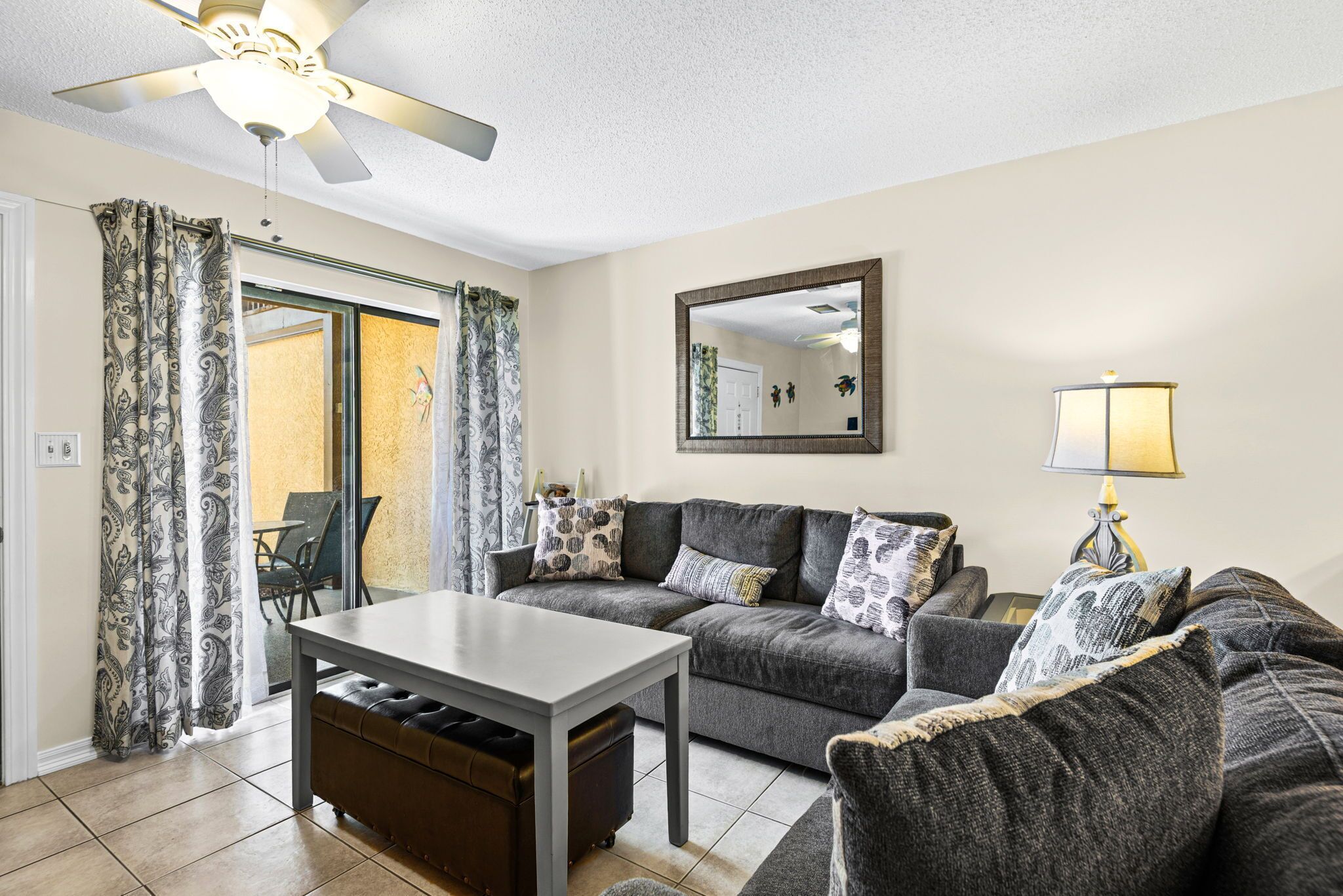 A living room with a sofa, a table, a ceiling fan, a mirror, and a lamp.
