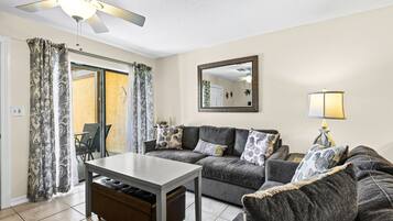 A living room with a sofa, a table, a ceiling fan, a mirror, and a lamp.