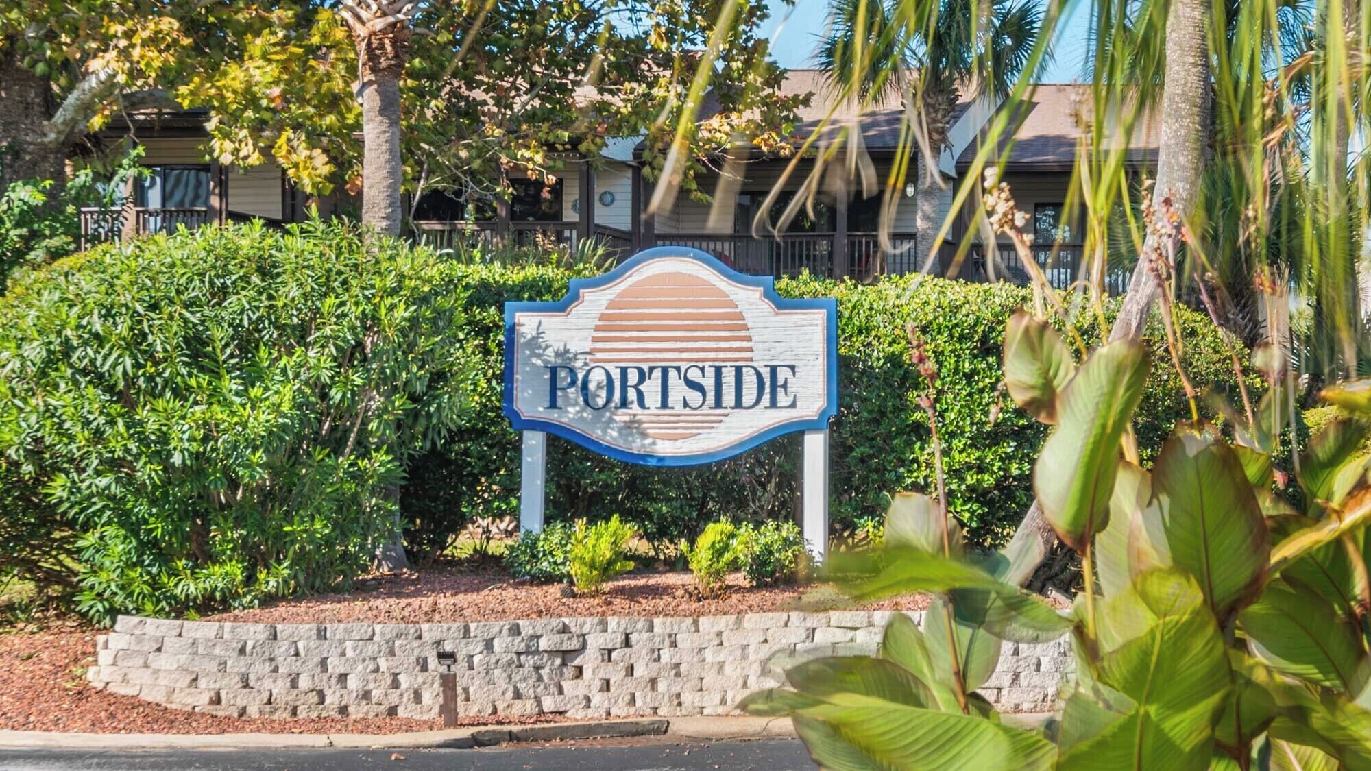 A sign with the word "PORTSIDE" surrounded by lush greenery and a stone wall.