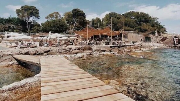 A wooden pathway leading to a rocky shoreline with clear water, a covered seating area, and trees in the background. - Le Bastidon Provençal T3 Terrace 3min from the Beach (Saint-Raphaël)