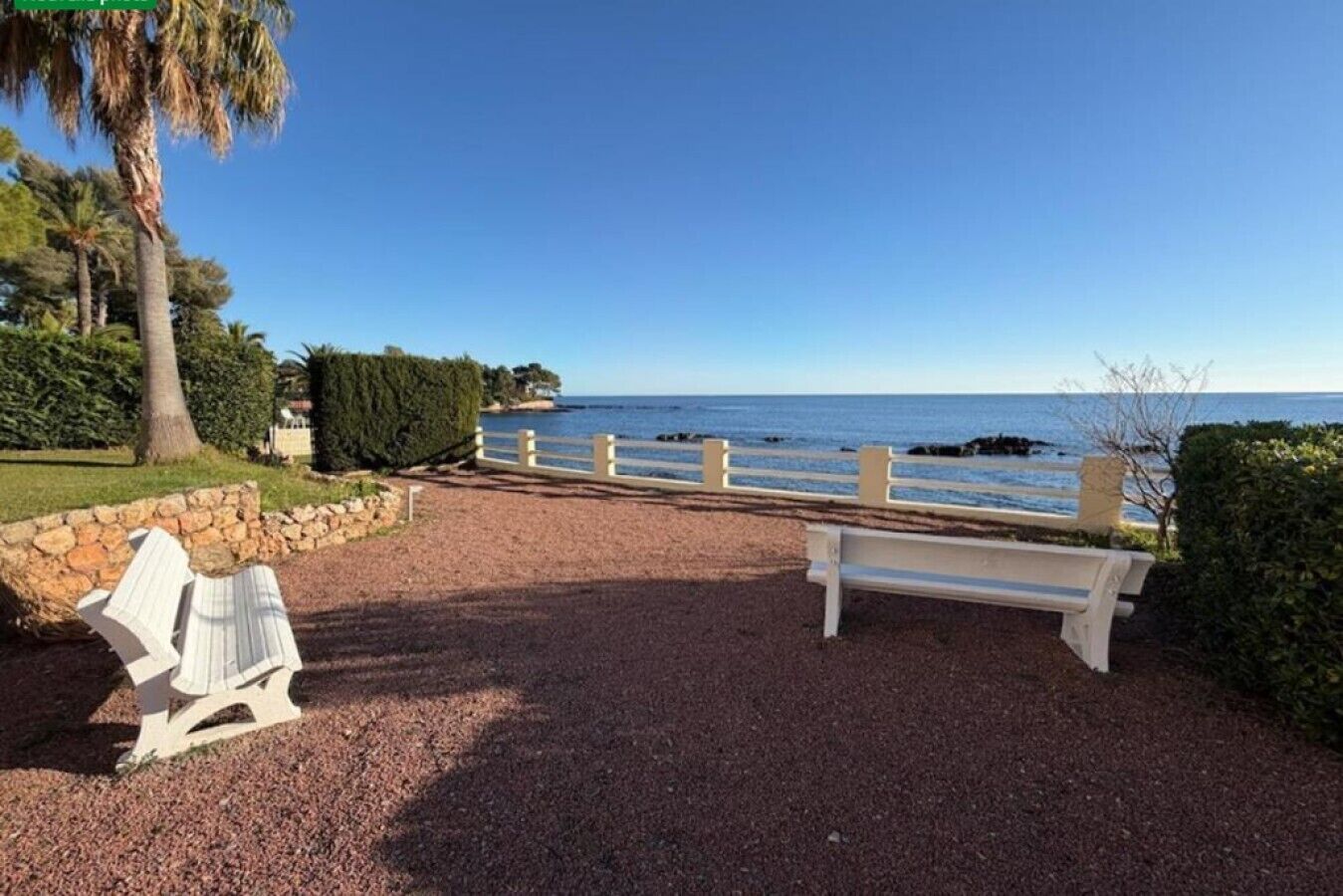 A gravel pathway leading to a bench overlooking a coastal area with a clear view of the sea and a stone wall on one side.