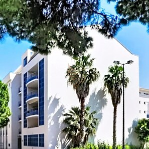Ein modernes Gebäude mit Balkonen, Palmen und blauem Himmel.