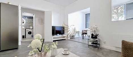 Una sala moderna con comedor, una cocina al fondo y un televisor.