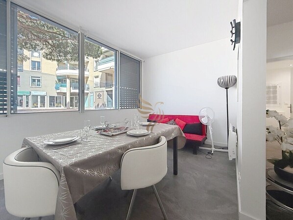 Un coin repas avec une table dressée pour quatre personnes, un canapé avec un coussin rouge et un ventilateur.