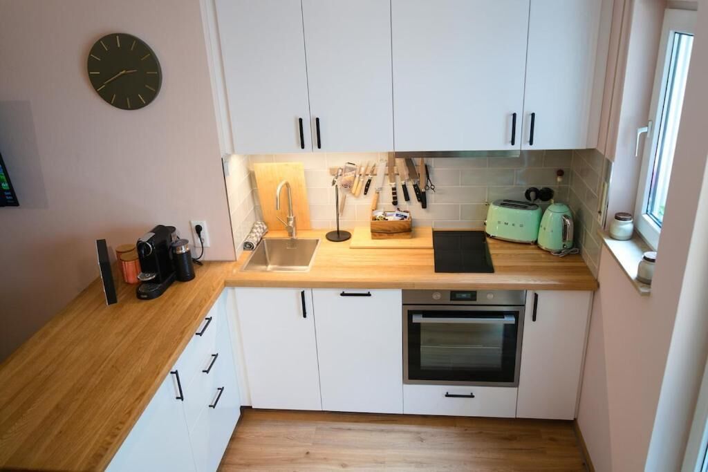 A compact kitchen with white cabinets, a wooden countertop, a sink, a toaster, and a clock on the wall.