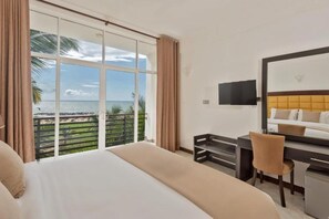 A hotel room with a large bed, a desk, a chair, a TV, and a balcony with a view of the ocean. - Beverly Beach Resort - Negombo (Negombo)