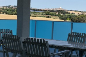 Una terrazza con tavolo e sedie, un muro blu e vista su un edificio e un paesaggio in lontananza.