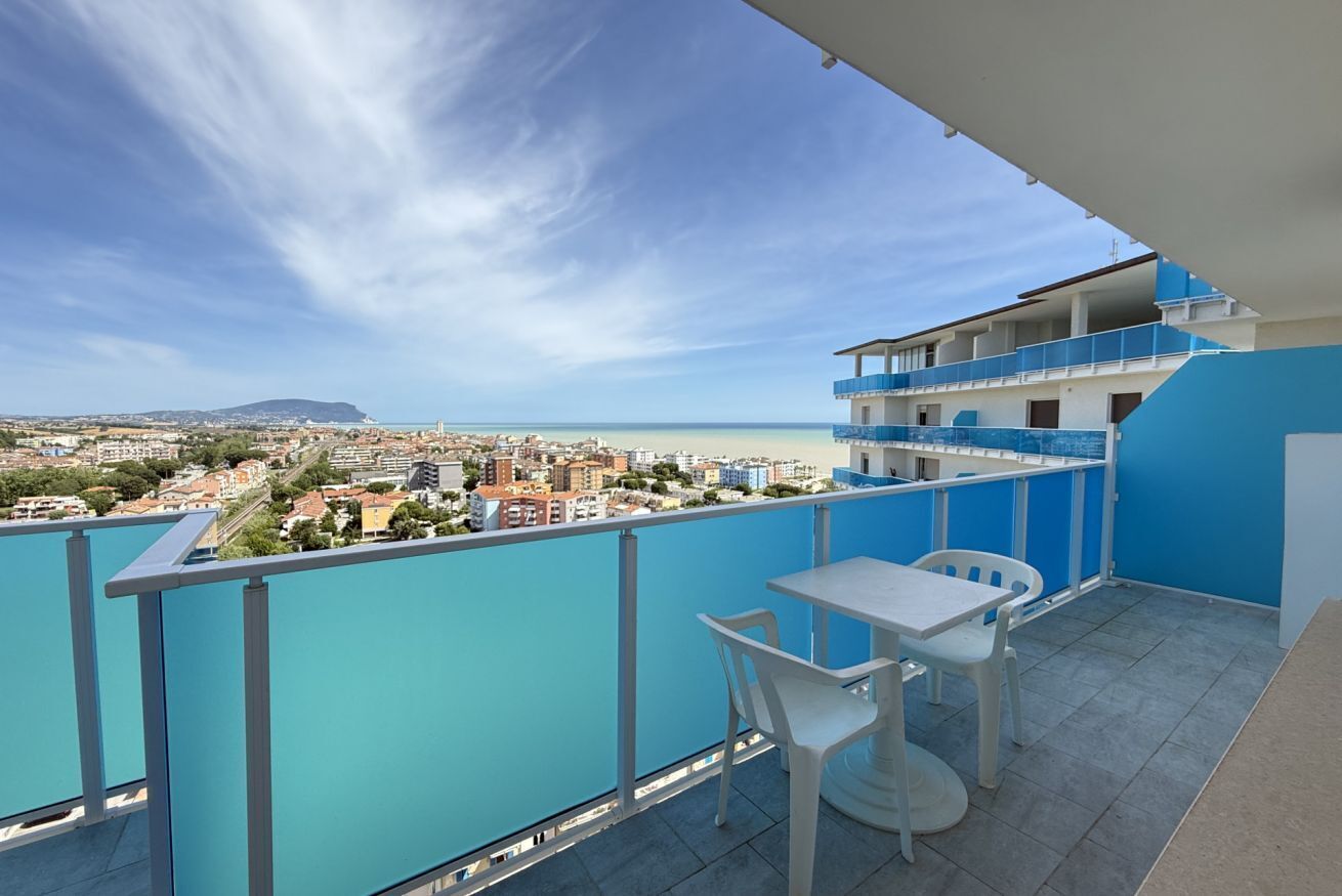 Un balcone con tavolo e sedie, affacciato su una città costiera.