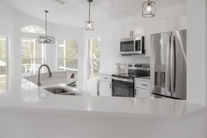 A modern kitchen with stainless steel appliances, white cabinetry, and pendant lighting.