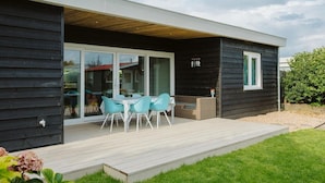 Una casa moderna con una terraza, un comedor con sillas y un gran ventanal corredizo.