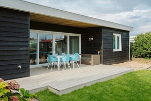 Ein modernes Haus mit einer Terrasse, einem Essbereich mit Stühlen und einer Schiebetür.