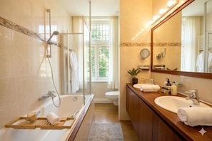 A bathroom with a bathtub, shower, toilet, and a large mirror.