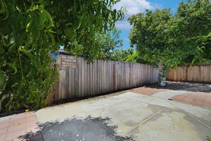 Un jardin avec une clôture en bois, une terrasse dallée et un arbre.