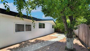 Una casa blanca con un patio empedrado, cerca de madera y un árbol.