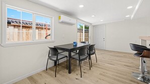 Una habitación con una mesa de comedor, cuatro sillas, una barra con un taburete y una ventana que da a una valla de madera.