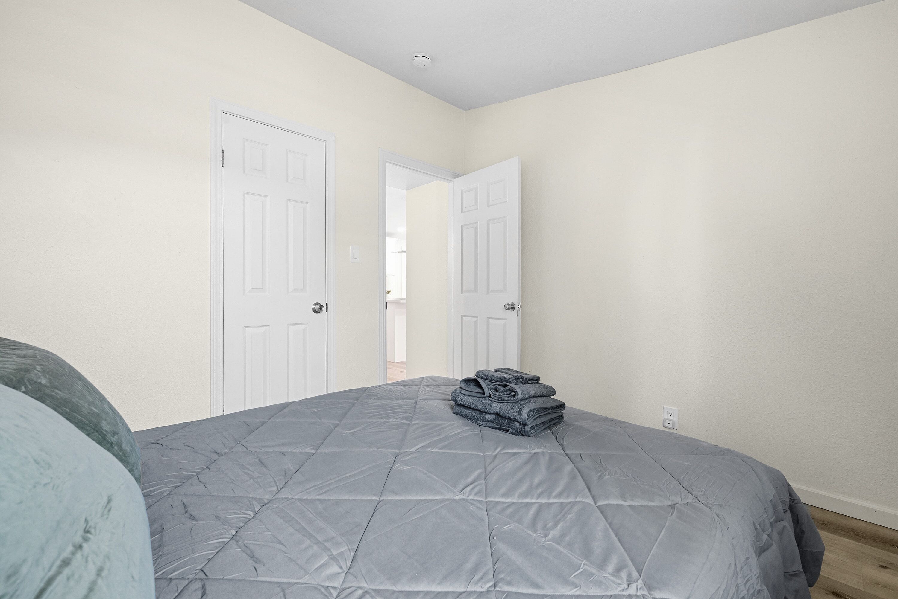 Une chambre à coucher avec un lit, deux portes blanches et un couloir visible.