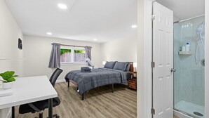 Un dormitorio con cama, mesita de noche, silla, escritorio y zona de ducha.