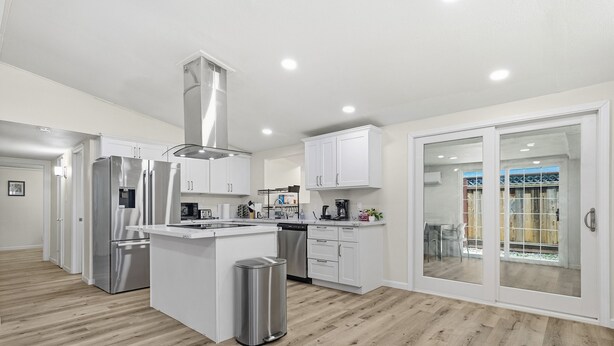 Una cocina moderna con electrodomésticos de acero inoxidable, una isla central y un ventanal corredero que da a un balcón.