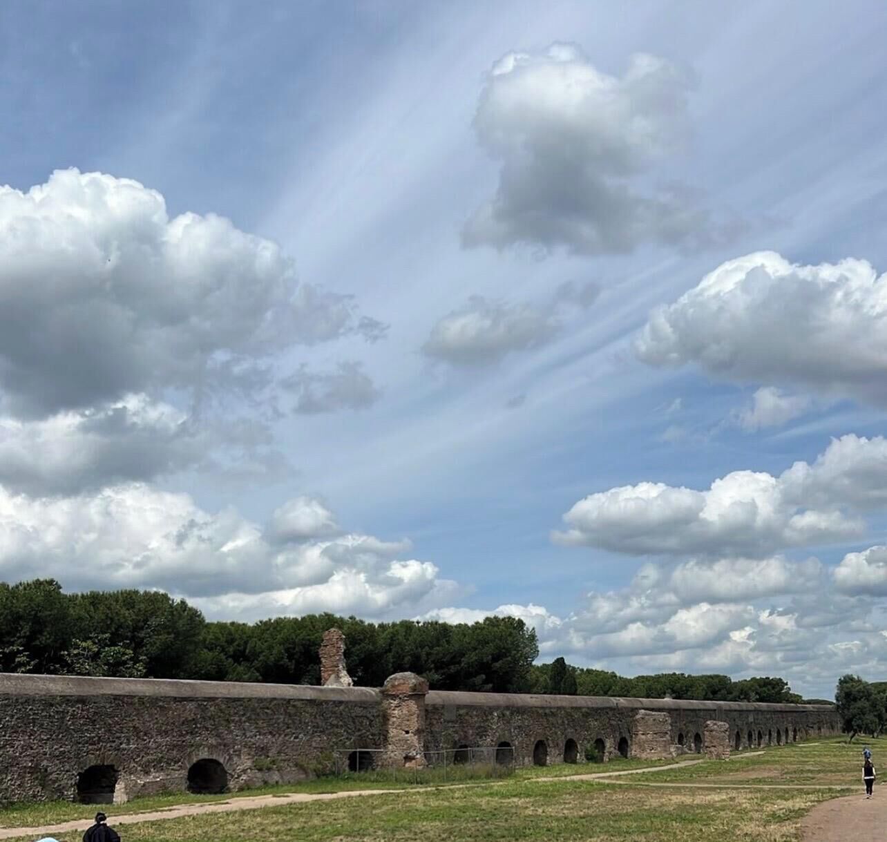 A historical stone structure with arches, a pathway, and a grassy area.