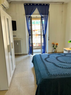 Un dormitorio con cama, un radiador, un televisor, una ventana con cortinas azules y vistas al exterior.