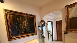 Een kamer met een beige bank, een groot schilderij in een lijst, een glazen kast en een spiegel.