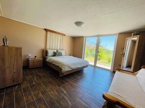 Une chambre à coucher comprenant un lit, des tables de chevet en bois, une commode et une porte-fenêtre coulissante donnant sur un balcon.