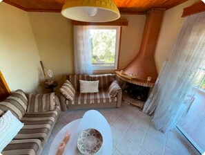 Una sala de estar acogedora con un sofá, una chimenea, un ventanal y suelo de baldosas.