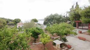 A garden with trees, a small building, and a paved area with benches. - Large Sea View Villa Near Athens Airport (Artemis)