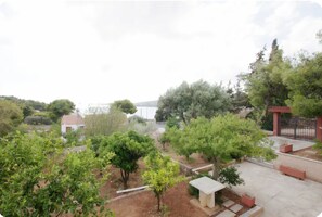 Un jardín con árboles, un edificio pequeño y una zona pavimentada con bancos.