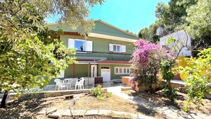 A two-story building with a patio area, outdoor seating, and a garden with flowering plants. - Large Sea View Villa Near Athens Airport (Artemis)