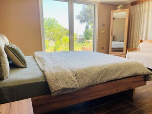Un dormitorio con cama, cabecera de madera, ventana grande y espejo.