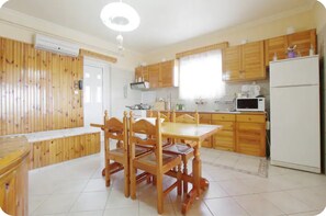 Une cuisine avec des meubles de rangement en bois, une table à manger avec des chaises, un réfrigérateur et un four à micro-ondes.