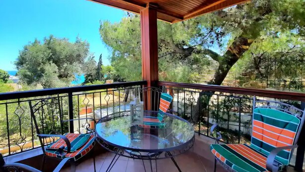 A covered balcony with a glass table and striped chairs, overlooking a garden and trees. - Large Sea View Villa Near Athens Airport (Artemis)
