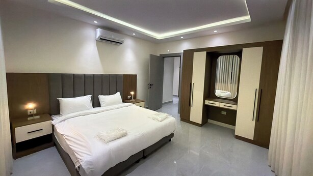 A modern hotel room with a large bed, bedside tables, a wardrobe, and an air conditioning unit. - 203 JRE Apartment With Stunning Boulevard Veiw (Amman)