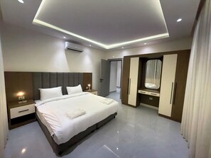 Quarto de hotel moderno com uma cama grande, mesas de cabeceira, guarda-roupa e ar condicionado.
