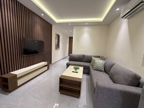 Uma sala de estar moderna com televisão de tela plana, um sofá cinza, uma mesa de centro de madeira e um banco embutido.