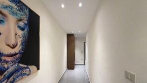 A hallway with a marble floor, a wooden door at the end, and a large abstract painting on the left wall. - 203 JRE Apartment With Stunning Boulevard Veiw (Amman)