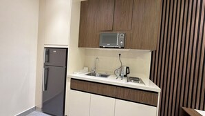 A compact kitchen with a refrigerator, microwave, sink, and wooden cabinets. - 203 JRE Apartment With Stunning Boulevard Veiw (Amman)