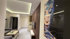 A modern interior with a sofa, a coffee table, a painting, and a kitchen area. - 203 JRE Apartment With Stunning Boulevard Veiw (Amman)