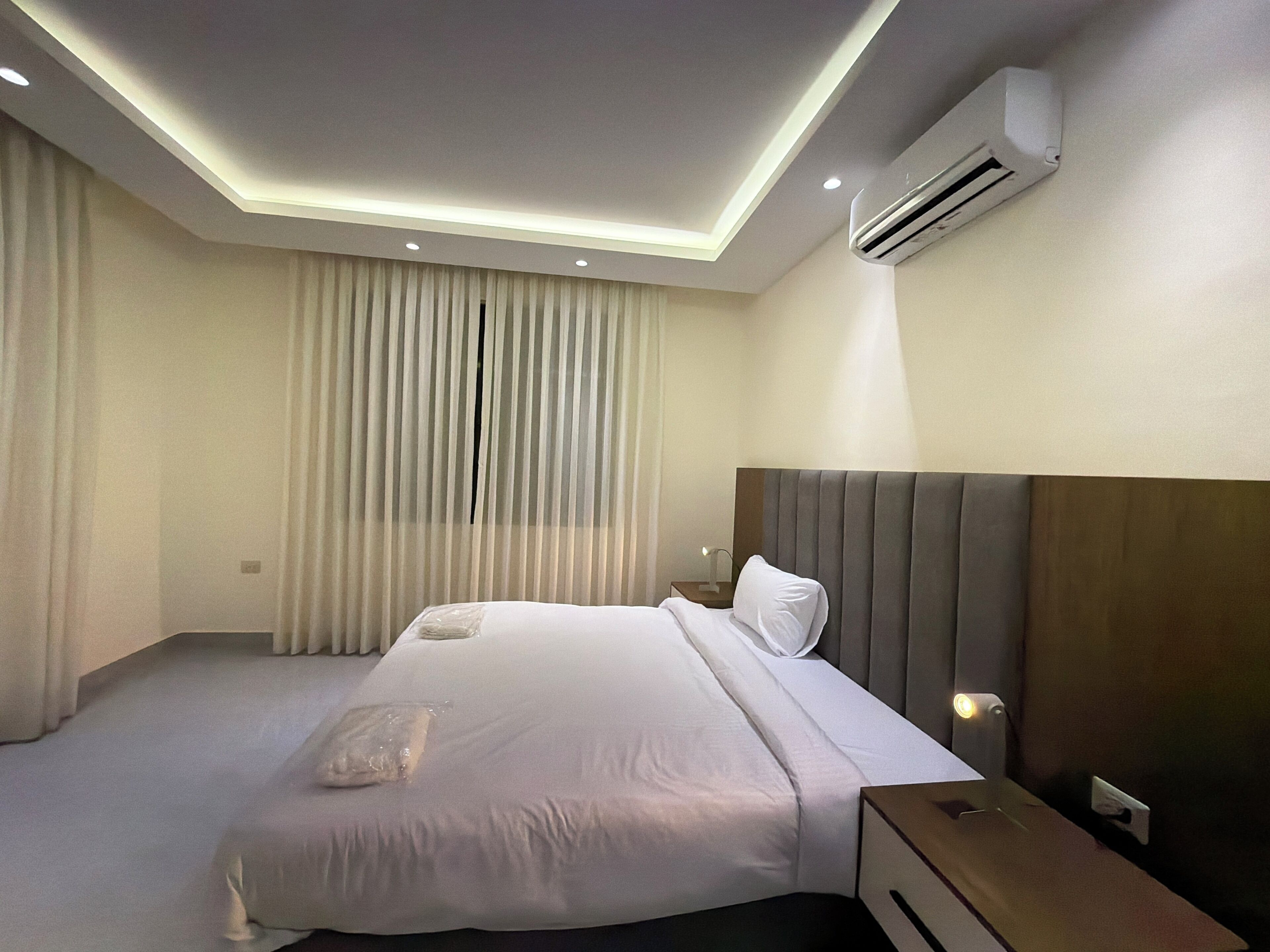 Ein modernes Hotelzimmer mit einem großen Bett, einem Nachttisch, einer Klimaanlage und einer Deckenleuchte.
