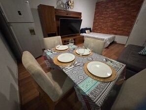 Un coin repas avec une table dressée pour quatre personnes, un téléviseur et un mur décoré d’un motif en briques.