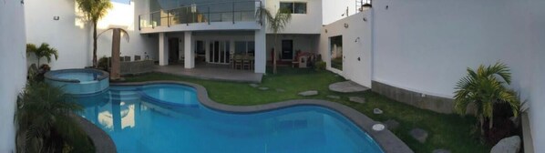 Un bâtiment moderne doté d’une piscine, d’un patio couvert et d’une pelouse bien entretenue.