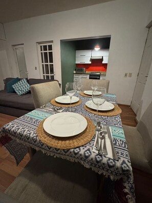 En matplats med ett bord dukat för fyra personer, en soffa och ett kök i bakgrunden.