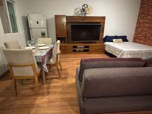 Ett kompakt bostadsutrymme med ett matbord, stolar, en soffa, en tv och en säng.