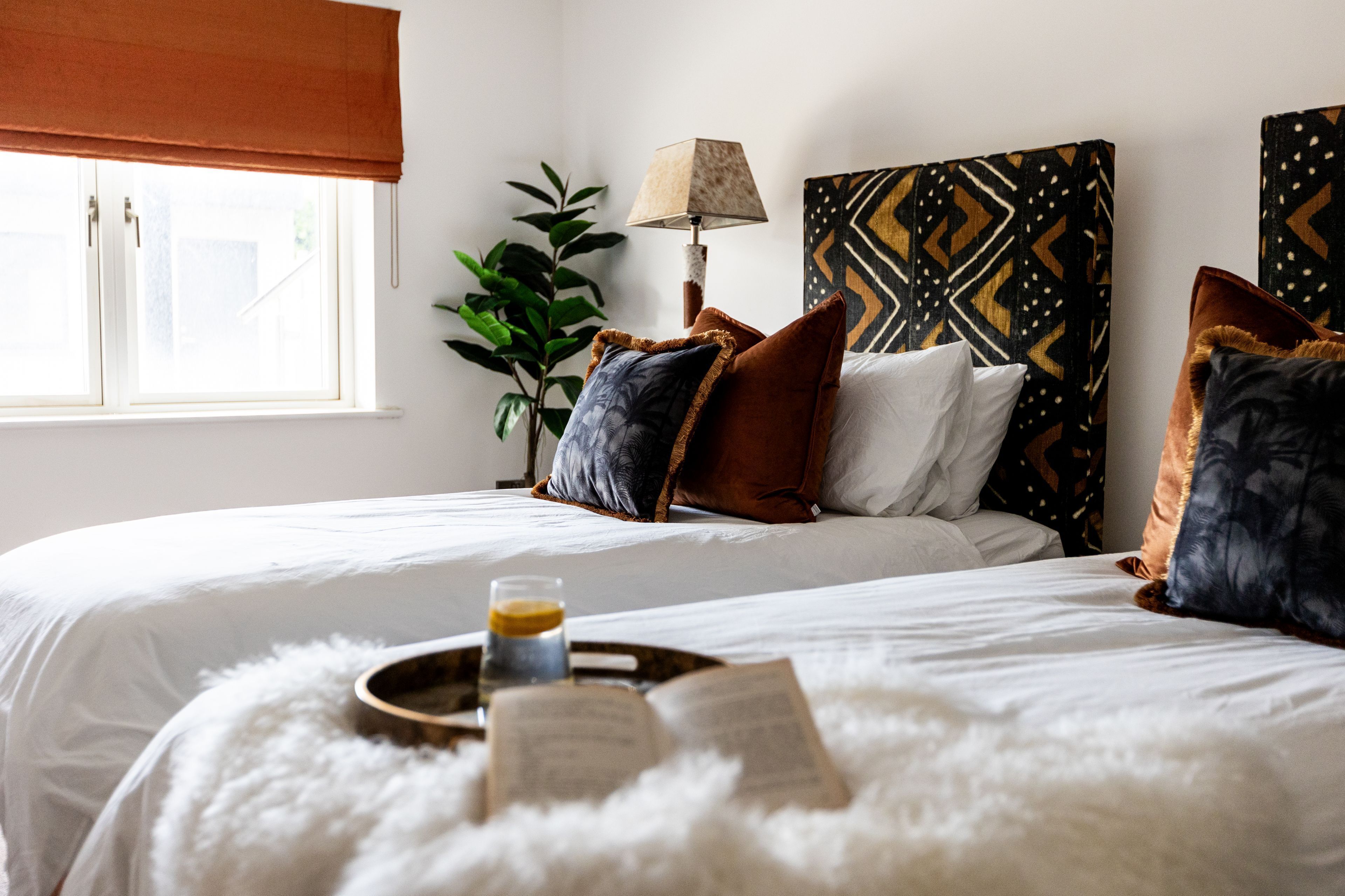 Habitación de hotel con cama, mesita de noche con un libro y un vaso, lámpara y ventana con vistas al exterior.