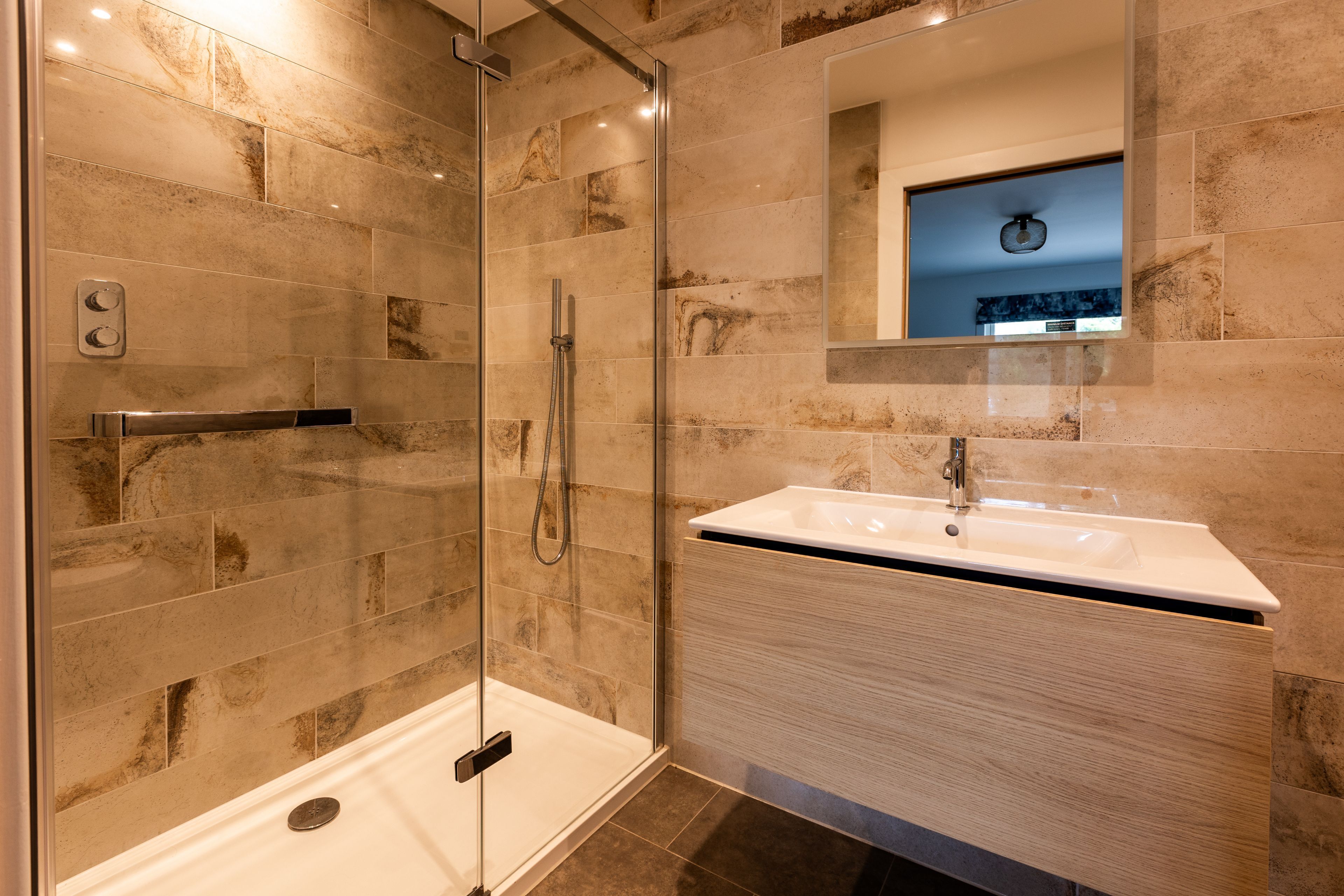 A modern bathroom with a glass-enclosed shower, a white sink, and a mirror above the sink.