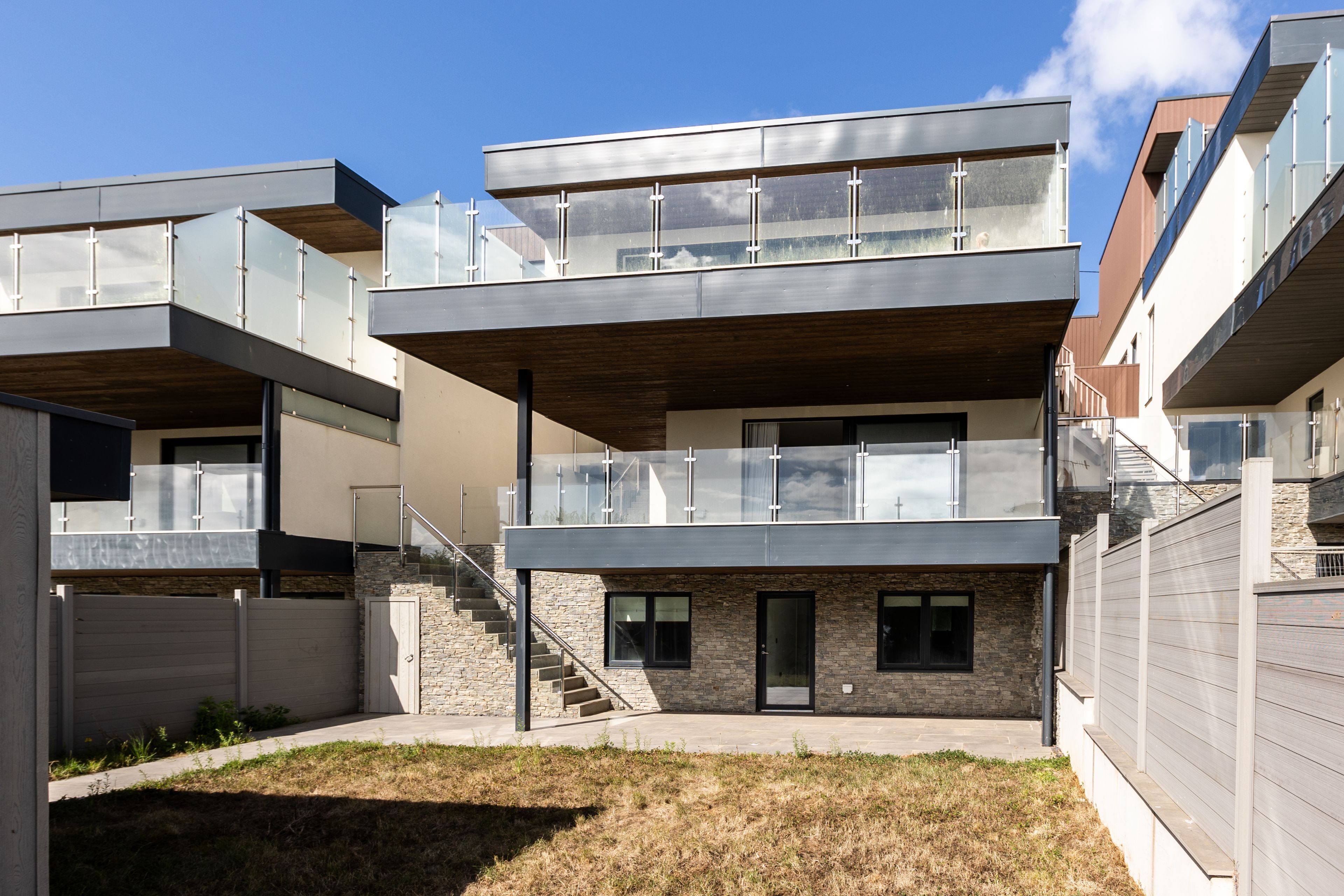 A modern multi-story residential building with a flat roof, large windows, and a stone facade.